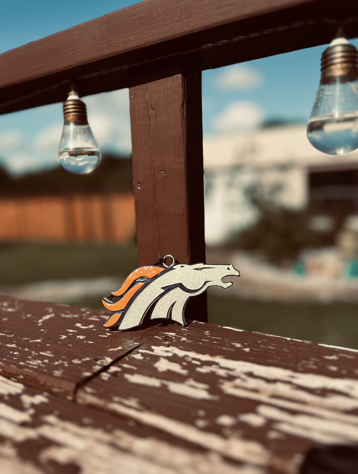 Wooden Denver Broncos logo on a weathered bench with bulbs hanging above.