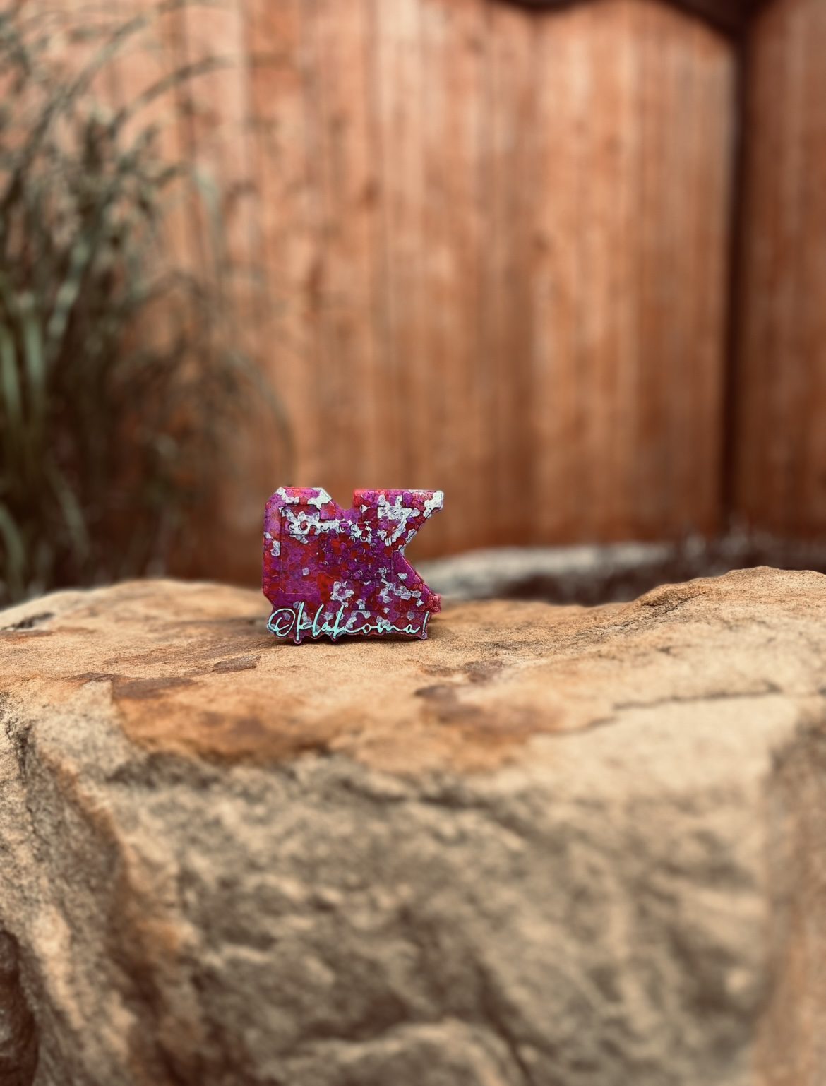 A small purple figurine of a dinosaur on a rock outdoors.