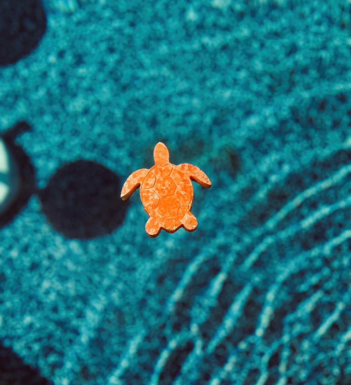 A small orange turtle toy floats in rippling blue water.