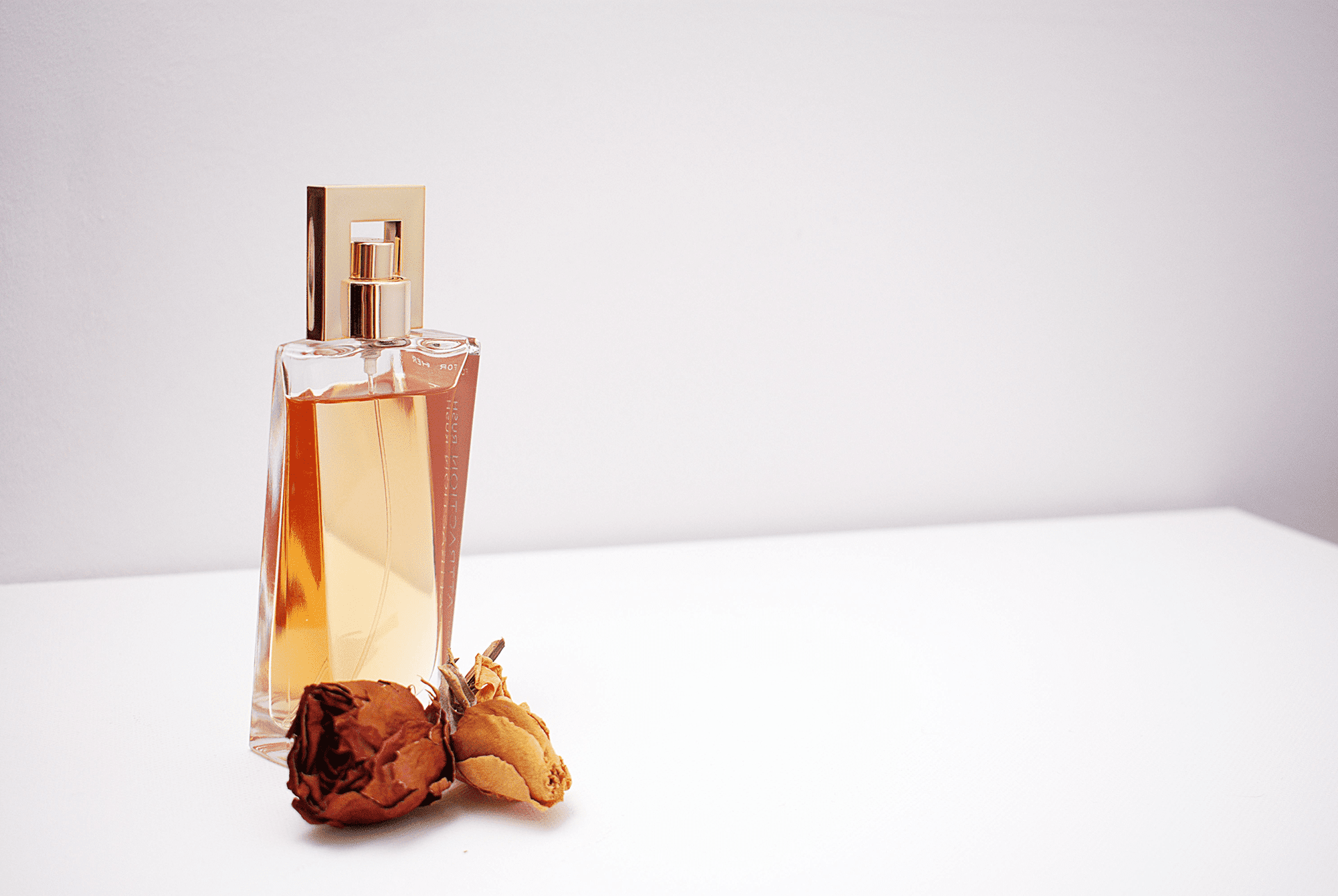 Elegant perfume bottle with dried roses on a white surface.