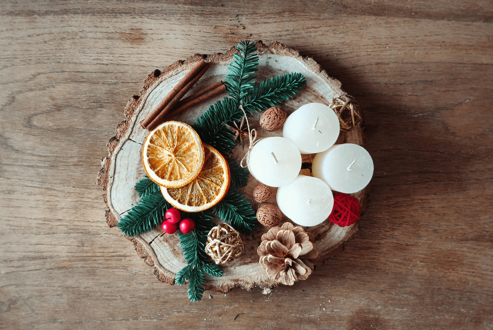 Festive arrangement with dried orange, pinecones, and candles on wood.
